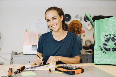 Porträt einer lächelnden Technikerin, die an einer Werkbank in einem kreativen Büro sitzt - MASF09324