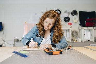 Confident redhead female engineer writing on wood at workbench in creative office - MASF09326