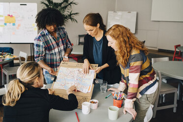 Multi-ethnic students showing map on placard to female manager at table in creative office - MASF09351