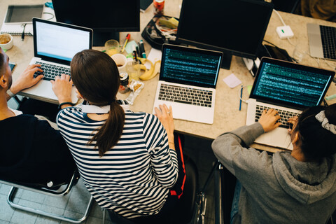 Blick von oben auf junge multiethnische Computerprogrammierer, die an Laptops am Schreibtisch in einem kleinen Büro programmieren, lizenzfreies Stockfoto