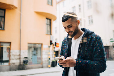 Selbstbewusster junger Geschäftsmann, der eine Textnachricht auf seinem Smartphone schreibt, gesehen durch ein Fenster - MASF09379