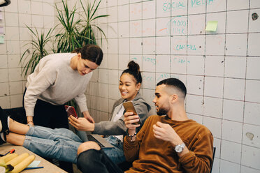 Young businesswoman sharing smart phone with colleagues while sitting at creative office - MASF09390