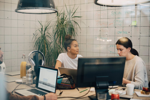 Multi-ethnische Hackerinnen arbeiten am Schreibtisch in einem kreativen Büro, gesehen durch ein Fenster - MASF09402