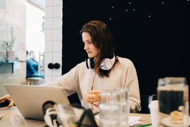 Young female computer programmer with headphones working while sitting at desk in small office - MASF09418