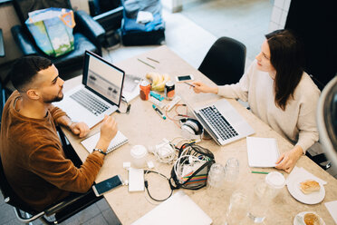 High angle view of male and female programmers discussing while sitting at desk in creative office - MASF09420