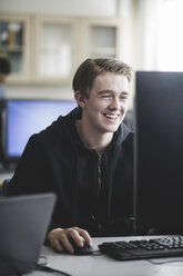 Smiling teenage boy using computer in classroom at high school - MASF09429