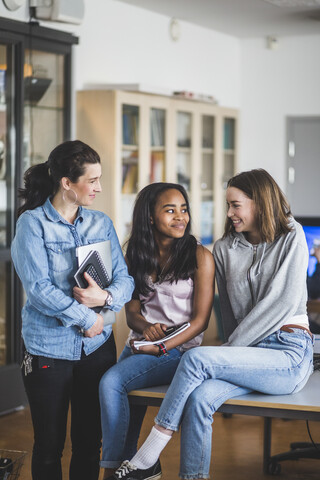 Lächelnde Lehrerin, die High-School-Schülerinnen und -Schüler am Schreibtisch im Computerraum beobachtet, lizenzfreies Stockfoto