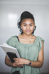 Porträt eines selbstbewussten Teenagers, der mit einem Buch vor einem Whiteboard im Computerraum einer High School steht - MASF09444