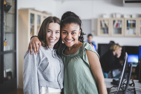 Portrait of smiling female teenage friends standing with arm around in computer lab at high school stock photo