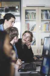 Selbstbewusste reife Lehrerin, die mit männlichen Schülern diskutiert, während sie auf den Computerbildschirm im Klassenzimmer schaut - MASF09452