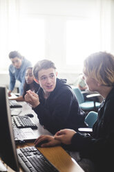 Männliche Gymnasiasten, die am Schreibtisch sitzend am Computer im Klassenzimmer diskutieren - MASF09454