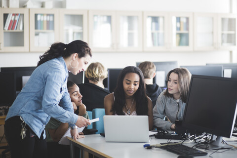 Reife Lehrerin, die Schülerinnen bei der Benutzung eines Laptops im Computerlabor einer High School hilft, lizenzfreies Stockfoto