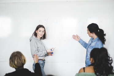 Mature teacher assisting teenage student while standing by whiteboard in classroom - MASF09465