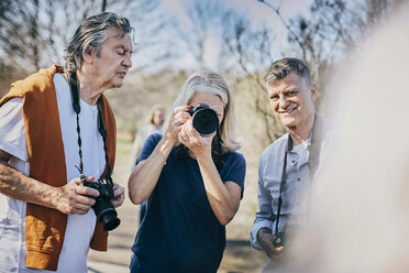 Senior woman using camera while standing with friends against bare trees at park - MASF09471