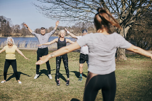 Rückansicht eines weiblichen Trainers, der ältere Menschen auf einem Feld im Park unterrichtet - MASF09475