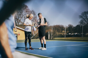 Älterer Mann und Frau mit Schlägern, die sich auf einem Tennisplatz unterhalten - MASF09478