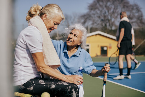 Ältere Frau im Gespräch mit müder Freundin auf dem Tennisplatz, lizenzfreies Stockfoto