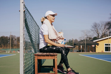 Seitenansicht einer müden älteren Frau, die auf einer Bank gegen den Himmel am Tennisplatz sitzt - MASF09482