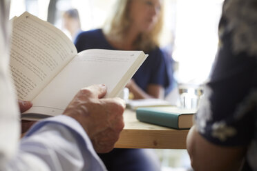 Ausgeschnittenes Bild eines älteren Mannes, der ein Buch liest, während er mit Freunden im Restaurant sitzt - MASF09491