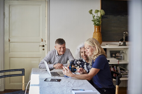 Glückliche ältere Männer und Frauen, die am Tisch im Wohnzimmer loggen, lizenzfreies Stockfoto