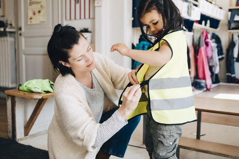 Lehrerin hilft einem Mädchen mit reflektierender Kleidung in der Garderobe einer Vorschule - MASF09539