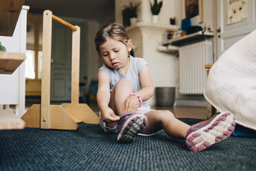 Mädchen in voller Länge auf Teppich sitzend und mit Schuhen in der Garderobe der Kinderbetreuung - MASF09540