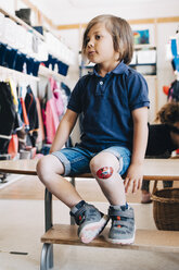 Full length of boy sitting on bench in cloakroom at preschool - MASF09544