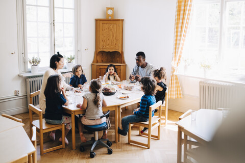 Teachers and students eating lunch at table in kindergarten classroom stock photo