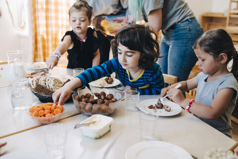 Schüler beim Mittagessen am Tisch gegenüber den im Klassenzimmer stehenden Lehrern, lizenzfreies Stockfoto