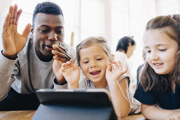 Playful teacher and female students looking at digital tablet in classroom - MASF09571