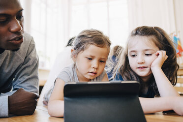 Mädchen benutzt digitales Tablet inmitten eines Freundes und eines männlichen Lehrers am Tisch im Klassenzimmer - MASF09574