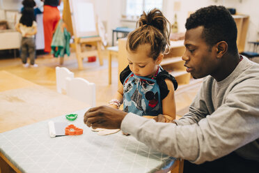 Mittlerer erwachsener männlicher Lehrer, der mit einem Mädchen am Tisch im Kinderbetreuungsraum spielt - MASF09575