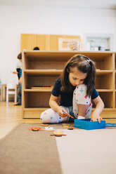 Mädchen in voller Länge, das mit Spielzeug spielt, während es auf dem Boden vor einem Regal in einem Klassenzimmer für Kinderbetreuung sitzt - MASF09577