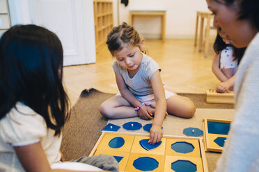 Lehrer und Schülerin betrachten ein Mädchen, das ein Puzzlespiel im Klassenzimmer spielt - MASF09578