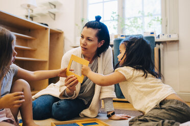 Lehrerin und Schüler halten einen Bilderrahmen, während sie im Klassenzimmer der Kinderbetreuung sitzen - MASF09580