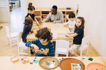 Hoher Blickwinkel des Jungen spielen mit Spielzeug gegen Freunde und Lehrer sitzen am Tisch im Klassenzimmer - MASF09584