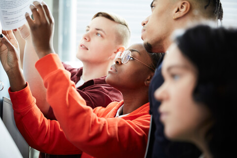 Männliche und weibliche Universitätsstudenten bei der Überprüfung von Testergebnissen an einer Pinnwand, lizenzfreies Stockfoto