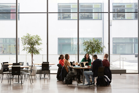 Studenten in voller Länge bei einem Gespräch am Tisch in der Universität, lizenzfreies Stockfoto