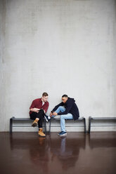 In voller Länge von männlichen Freunden mit Technologien sitzen auf Bank gegen die Wand in der Universität - MASF09634
