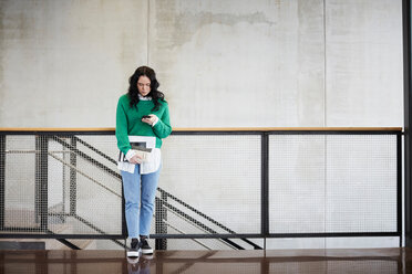 Full length of student using mobile phone while standing at railing against wall in university - MASF09639