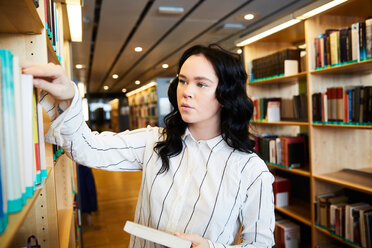 Young female student searching book in university library - MASF09661