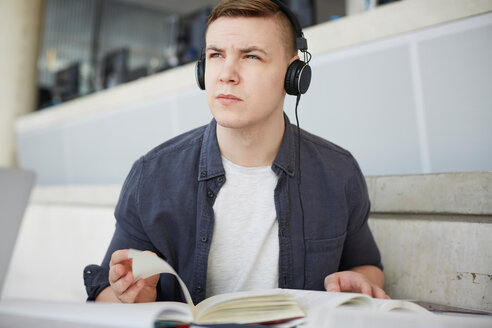 Junge Studentin mit Kopfhörern blättert beim Lernen am Tisch in der Universität - MASF09667