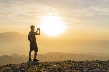 Spain, Barcelona, Natural Park of Sant Llorenc, man hiking and taking a picture of the view at sunset - AFVF01889