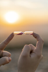 Close-up of man's hand holding an hourglass at sunset - AFVF01896