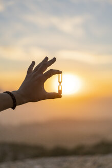 Nahaufnahme einer Männerhand, die eine Sanduhr bei Sonnenuntergang hält - AFVF01898