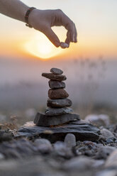 Nahaufnahme einer Männerhand, die bei Sonnenuntergang einen Stein auf einen Steinhaufen legt - AFVF01904
