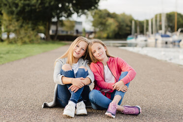 Portrait of two smiling girls sitting head to head on the ground - NMSF00277