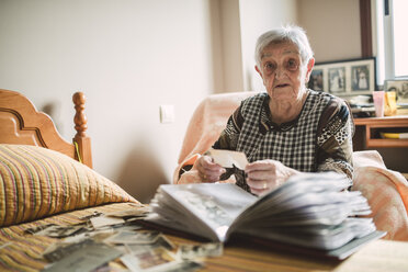 Porträt einer älteren Frau, die zu Hause alte Fotos in ein Fotoalbum einträgt - RAEF02217