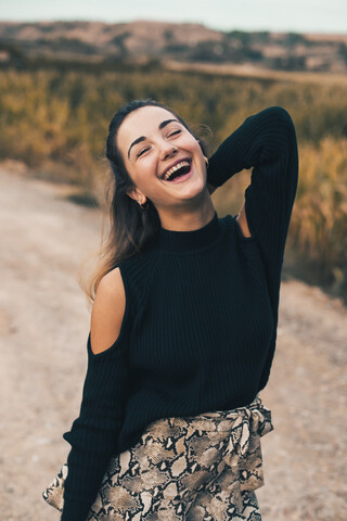 Porträt einer lachenden jungen Frau in der Natur, die einen modischen schwarzen Pullover trägt, lizenzfreies Stockfoto