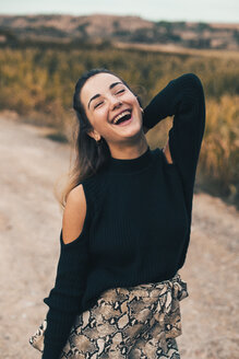 Porträt einer lachenden jungen Frau in der Natur, die einen modischen schwarzen Pullover trägt - ACPF00366
